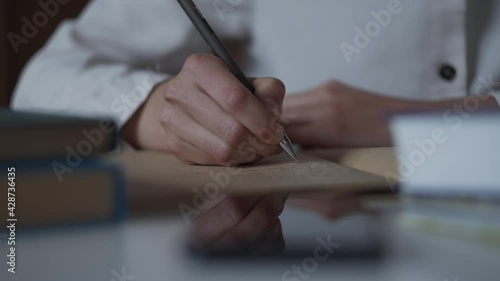 Macro view of female hand writing notes in vintage sketchbook notebook diary. Education concept woman sits at table with books, studies. Hand is reflected on table. Create Wish list. Diary of memories