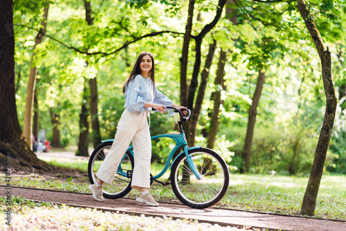 Joyful woman walking at park with bike in hands © WellStock