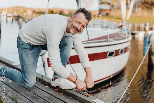 Billede på lærred Attractive sporty man tying up the mooring rope of his yacht