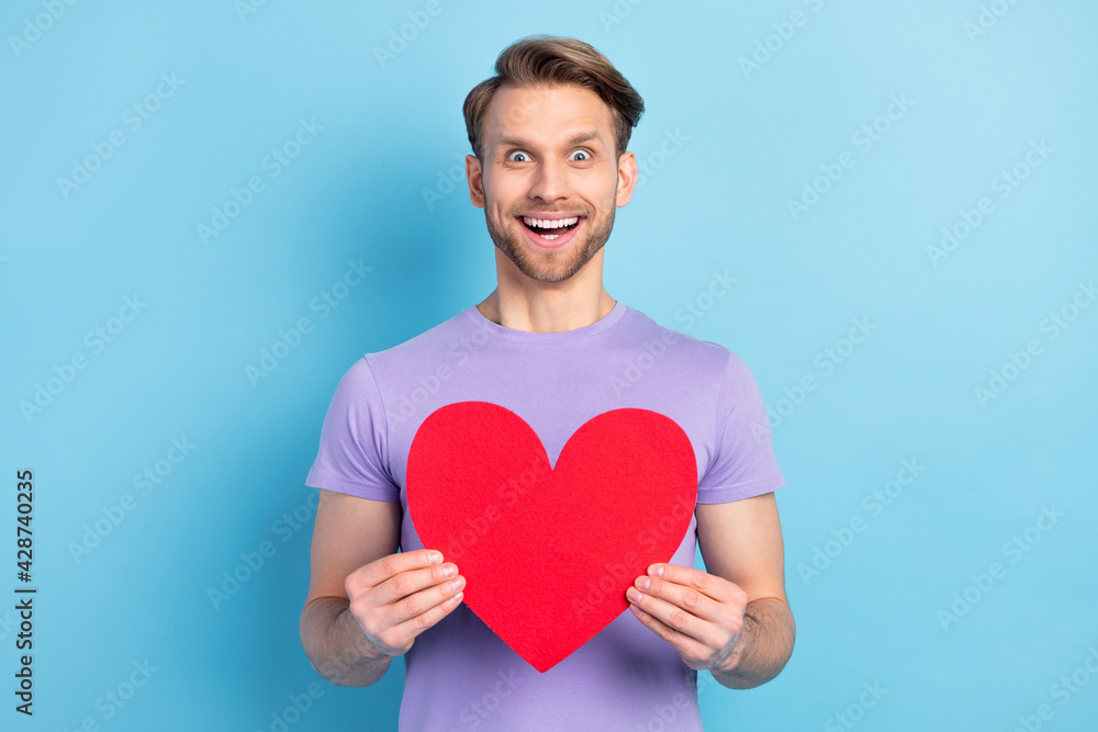 Photo portrait of young man amazed showing red heart isolated on pastel blue color background Photo portrait of young man amazed showing red heart isolated on pastel blue color background