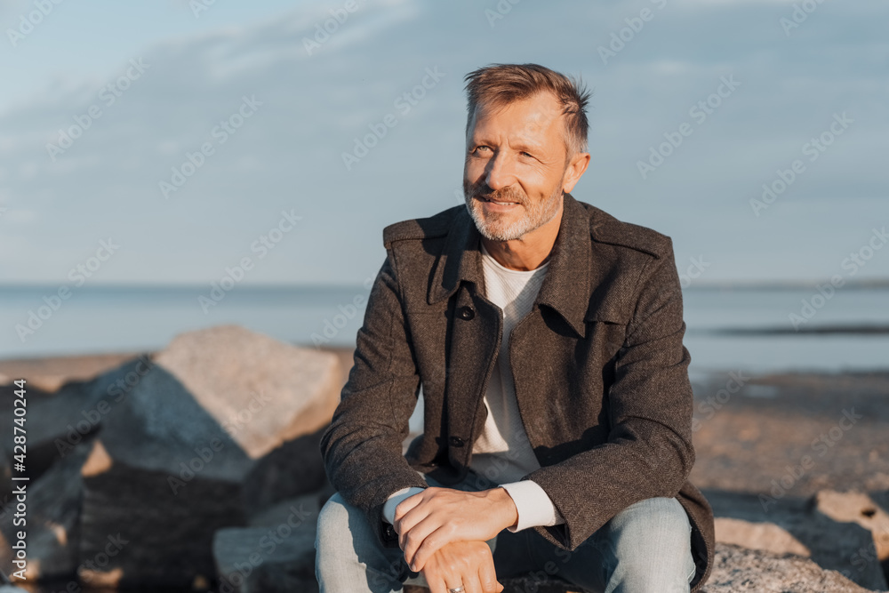 Attractive trendy man relaxing at the seaside at sunset Attractive trendy man relaxing at the seaside at sunset