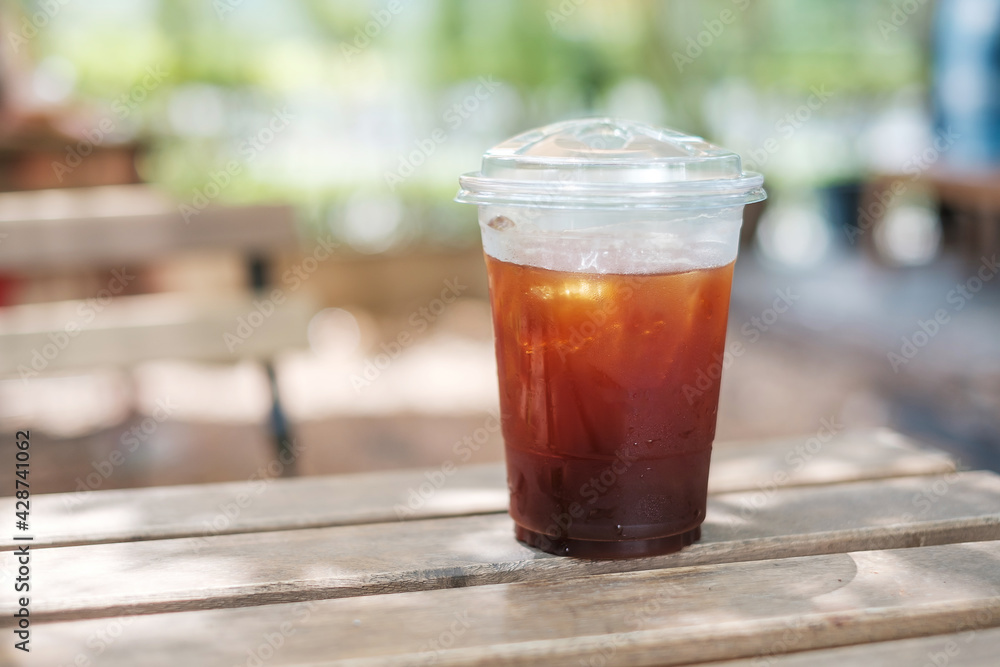 Iced americano coffee cup on wooden table against nature background at cafe