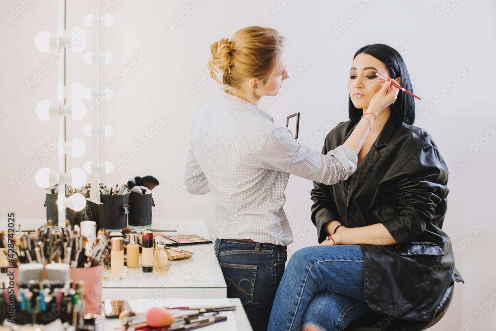 Makeup master doing makeup to beautiful model indoor beauty studio