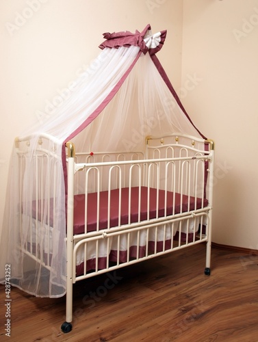 White metal four-poster bed for a newborn baby in the interior of the room. Baby cot. © Uliana