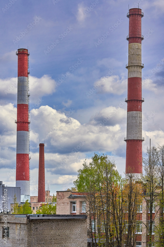 Tall factory chimneys against backdrop of a cloudy sky and residential buildings Tall factory chimneys against backdrop of a cloudy sky and residential buildings