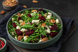 Beet or beetroot salad with fresh arugula, blue cheese and pecan nuts in a plate on black background. close up