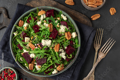 Salad with fresh arugula, beetroot, gorgonzola cheese and pecan nuts in a plate with fork on black background. top view.