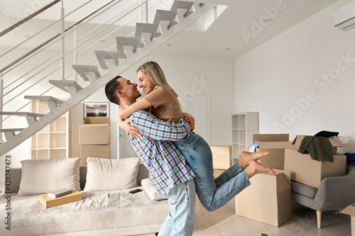 Happy independent couple first time home owners hugging in living room on moving day. Young man and woman apartment buyers celebrating relocation, removal, mortgage, new house purchase concept.