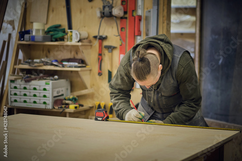 Carpenter holding a measure tape on the work bench. Woodwork and furniture making concept. Carpenter in the workshop marks out and assembles parts of the furniture cabinet
