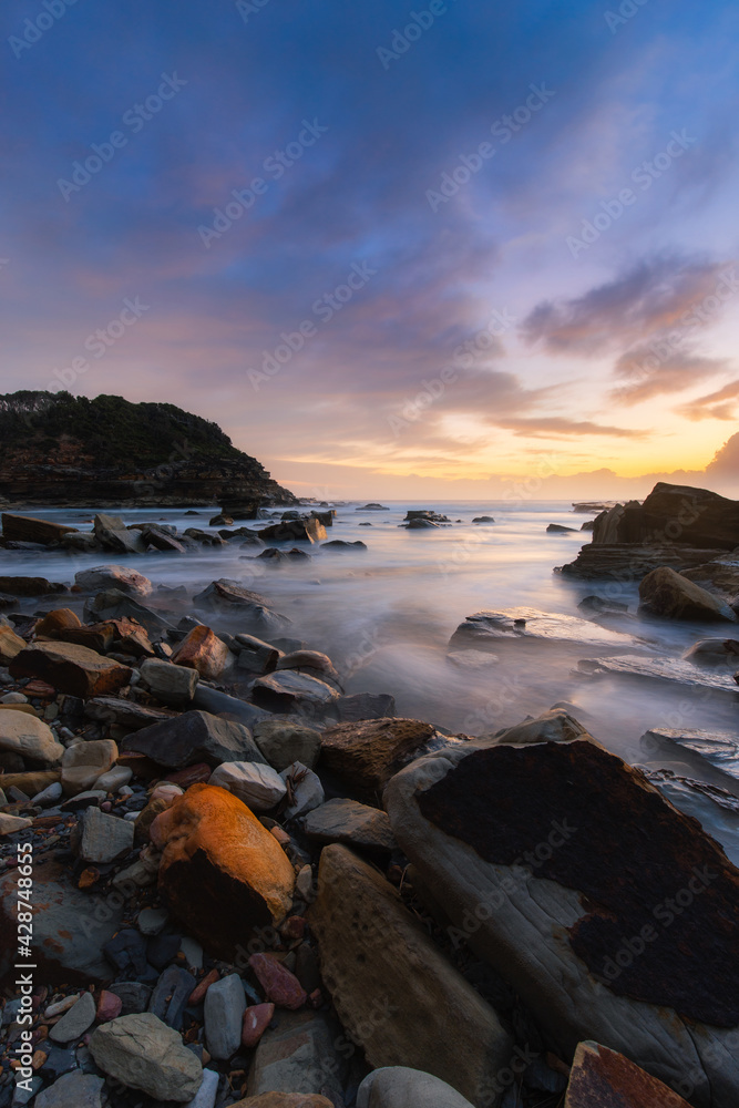 Sunrise view of rocky beach shore with water flowing.