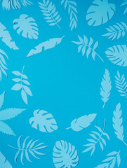 Natural tropical frame with blue paper palm leaves on pastel blue background. Minimal summer exotic texture concept with copy space for text. Flat lay, top view.