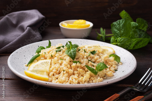 Boiled bulgur with fresh lemon and mint on a plate. A traditional oriental dish called Tabouleh. dark wooden background.