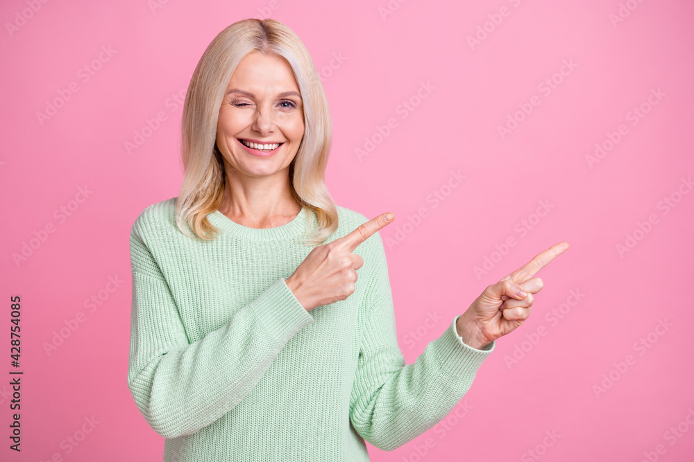 Photo portrait of woman blonde hair winking pointing finger blank space isolated on pastel pink color background