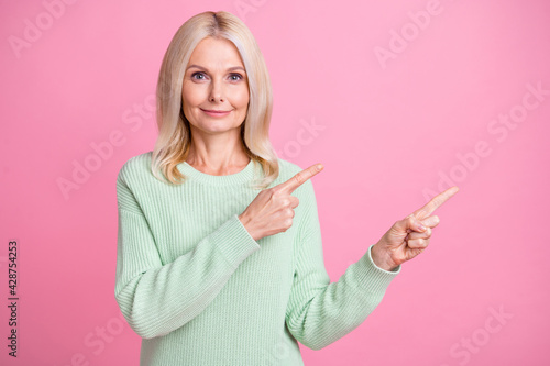 Photo portrait of elderly lady pointing two fingers at blank space isolated on pastel pink colored background
