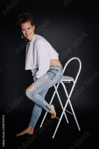 Portrait Frau, kraftvoll, Fitness, dunkler Hintergrund, zerissene Jeans auf Sessel, weißer Pulli, Bauchfrei
