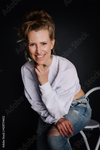 Portrait Frau, kraftvoll, Fitness, dunkler Hintergrund, zerissene Jeans auf Sessel, weißer Pulli, Bauchfrei