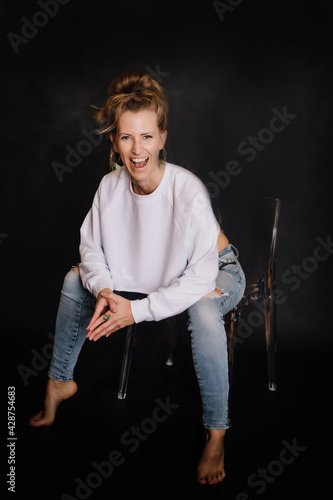 Portrait Frau, kraftvoll, Fitness, dunkler Hintergrund, zerissene Jeans auf Sessel, weißer Pulli, Bauchfrei