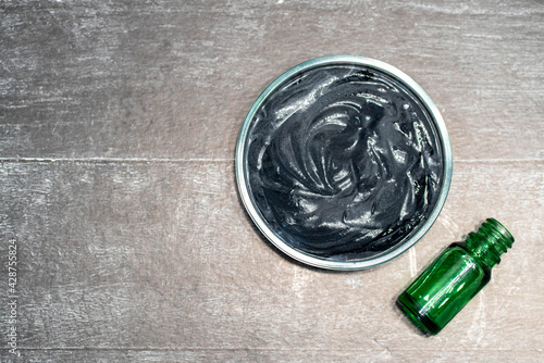 Homemade face mask and scrub with activated carbon powder and yogurt on wooden background with green glass bottle