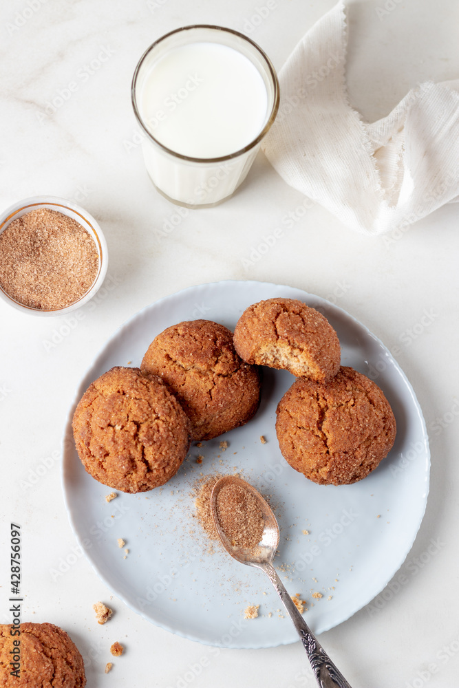 Freshly Homemade baked ginger cookies with cinnamon and sugar on gray plate and glass of milk, light marble background. Freshly Homemade baked ginger cookies with cinnamon and sugar on gray plate and glass of milk, light marble background.