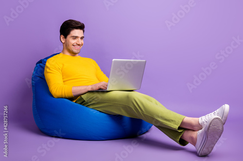 Full size profile portrait of positive guy sit big soft chair hold netbook working isolated on purple color background