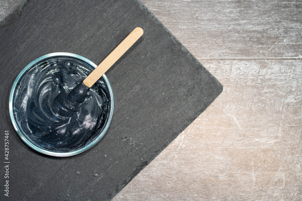 Homemade face mask and scrub with activated charcoal powder and yogurt with stick on black slate platter Homemade face mask and scrub with activated charcoal powder and yogurt with stick on black slate platter