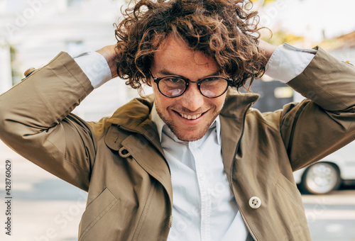 Fotografie A young successful businessman in eyewear smiling broadly posing outdoors