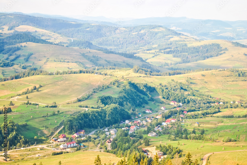 Summer landscape with village in valley and mountain in Carpathians, Ukraine. Tranquil scenery, soft focus