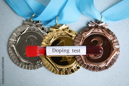 Medals and tube of blood with words Doping test on light blue background, flat lay photo