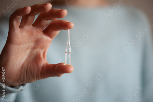 Aged woman holding glass bottle with medicine close up over blue. Healthcare lifestyle. Influenza treatment.