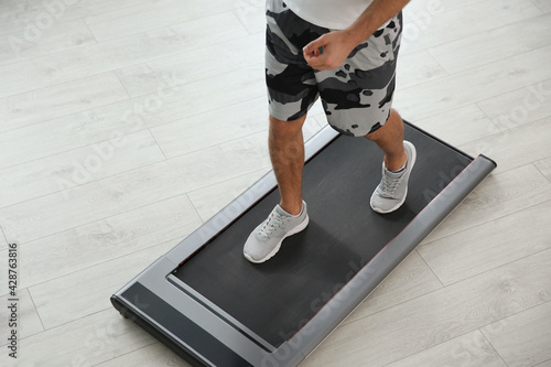 Sporty man training on walking treadmill at home, closeup