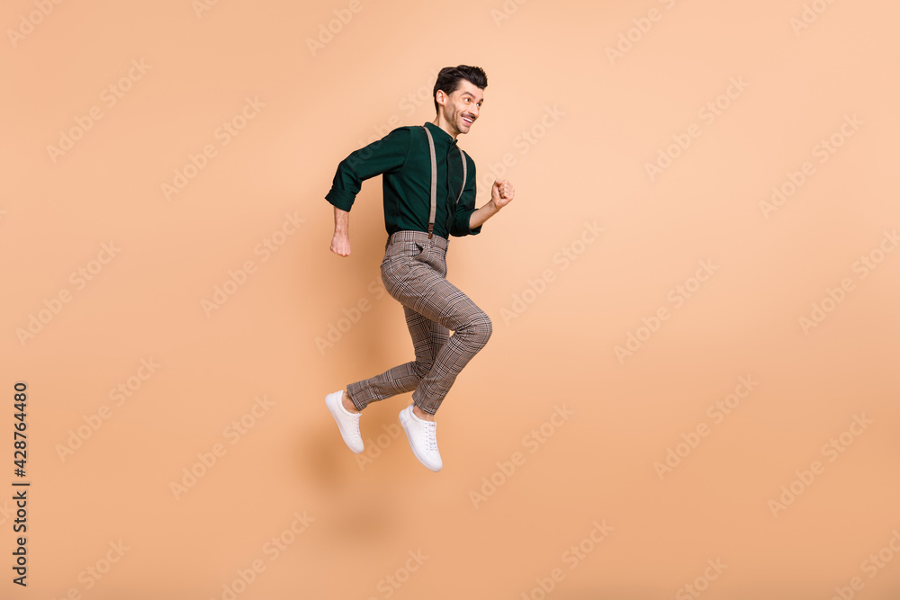 Full length profile side photo of young man jump up run empty space sale hurry isolated on beige color background Full length profile side photo of young man jump up run empty space sale hurry isolated on beige color background