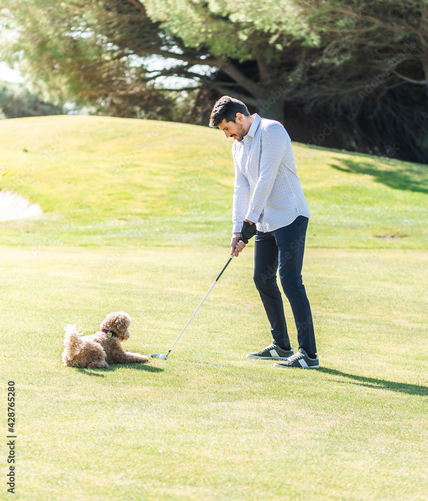 A young Caucasian male in a golf cart with his Goldendoodle puppy on a professional golf course