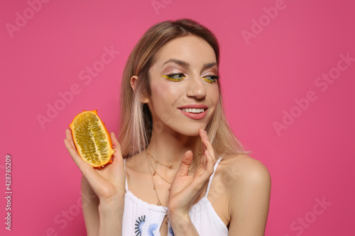 Young woman with fresh kiwano on pink background. Exotic fruit