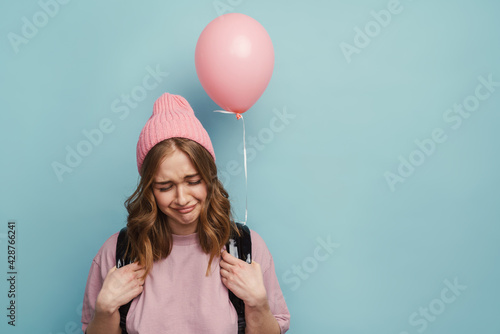 Fototapeta Young white student girl with backpack frowning and posing with balloon