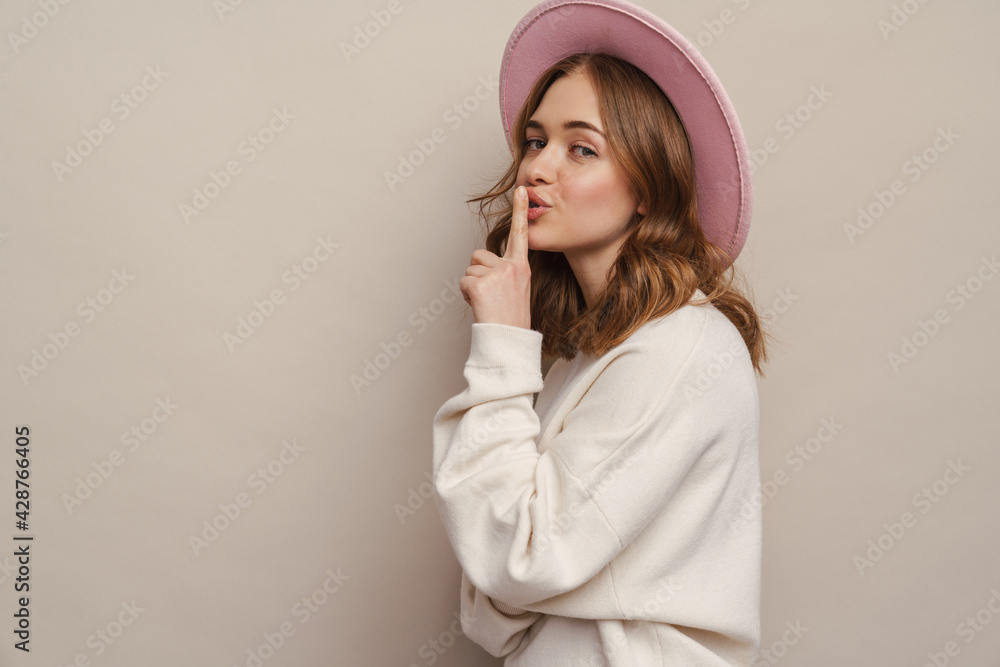 Young happy woman in hat showing silence gesture at camera Young happy woman in hat showing silence gesture at camera