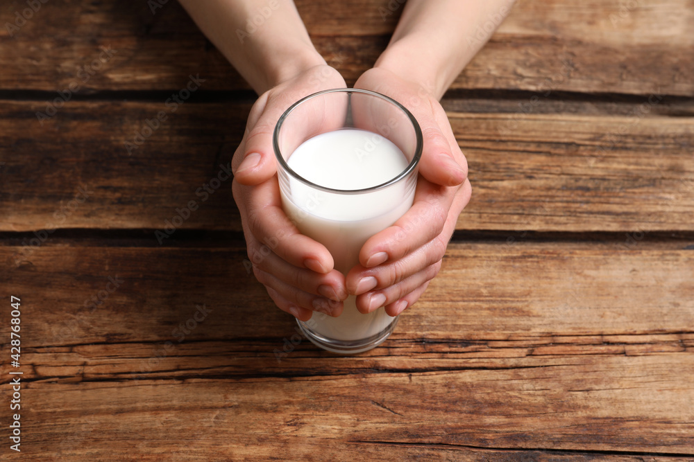 Woman holding glass of milk at wooden table, closeup - obrazy, fototapety, plakaty 