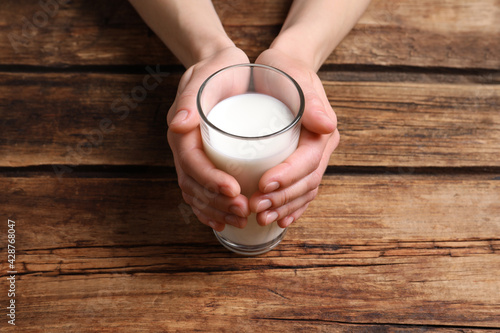 Woman holding glass of milk at wooden table, closeup