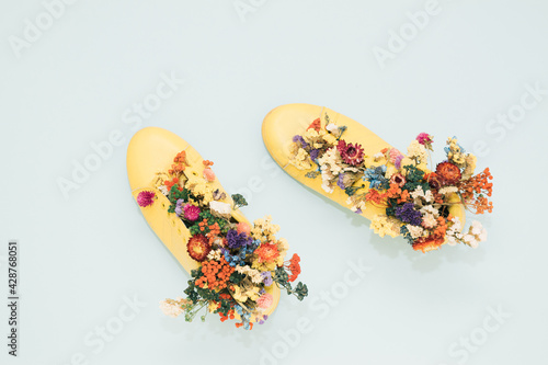 Yellow sneakers on a pastel blue background filled with flowers. Spring minimal koncept. Flat lay. 