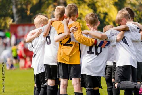 Fototapeta Naklejka Na Ścianę i Meble -  Group of happy sports boys huddling in a team. Happy school kids play sports together. Children motivating each other before playing a soccer football game. Sports Competition for Youth