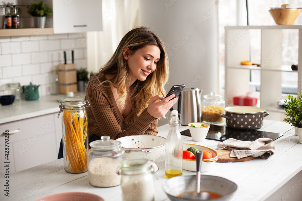 Young woman in kitchen. Beautiful woman using phone while making food.. Young woman in kitchen. Beautiful woman using phone while making food..