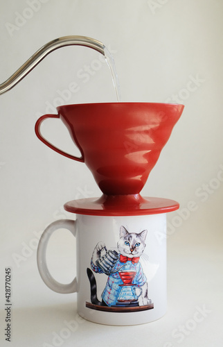 Manual V60 coffee brewing method. Water pours from a gooseneck kettle into red dripper on mug with barista cat print. White background. Specialty coffee aesthetics concept