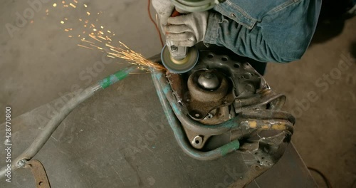 Locksmith sands the unfinished decorative metal steampunk fish sculpture by electric grinder with a lot of sparks in slow motion, metalwork at workshop, 4k 60p Prores HQ photo