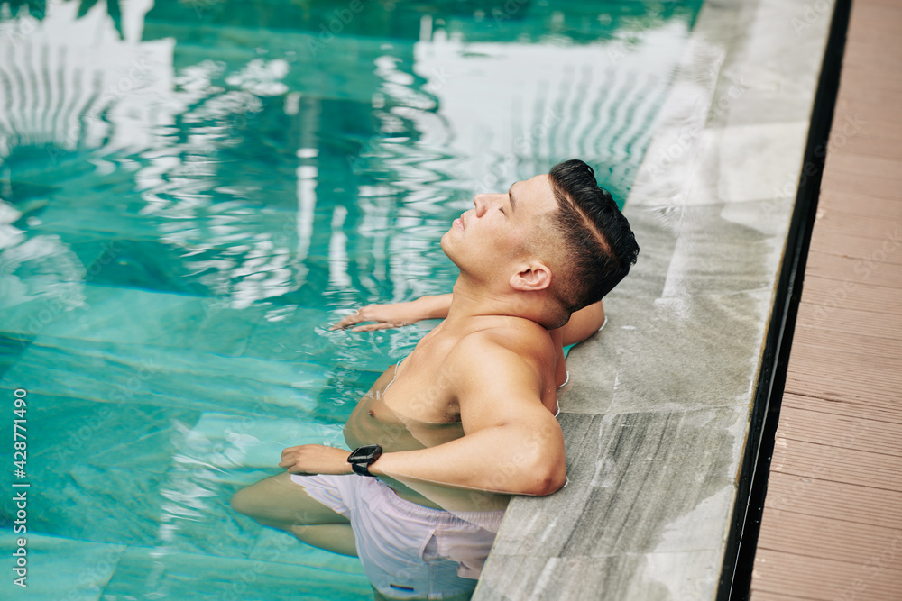 Mature fit man relaxing and refreshing in swimming pool on hot summer day