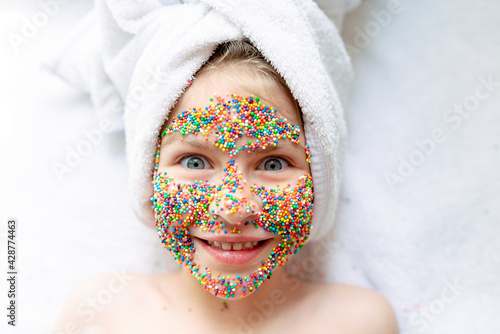 Fototapeta Naklejka Na Ścianę i Meble -  Portrait of cute  little girl with a face mask made of Easter decoration smiling with a towel on her had, cosmetics for children