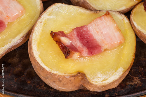 Potato half baked with bacon slice on baking sheet closeup