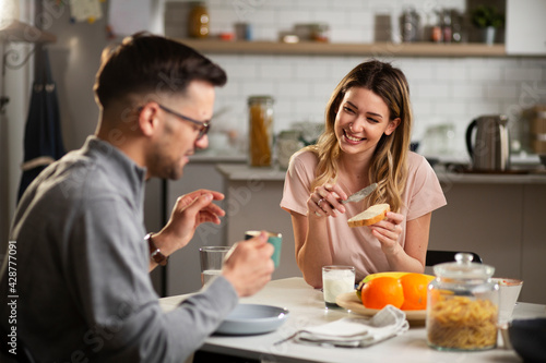 Beautiful young woman enjoying in breakfast with boyfriend. Happy young couple drinking coffee and eating sandwich at home..