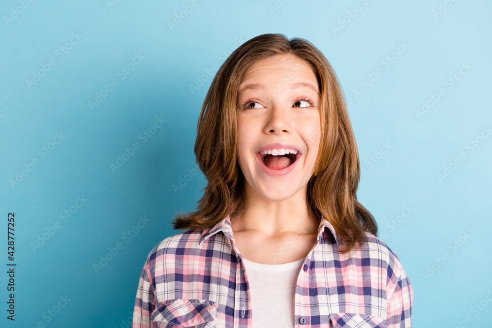 Photo of funky pretty small girl wear checkered shirt smiling open mouth looking empty space isolated blue color background Photo of funky pretty small girl wear checkered shirt smiling open mouth looking empty space isolated blue color background