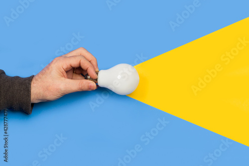 Mano de hombre sosteniendo una bombilla sobre un fondo azul y amarillo. Vista superior y de cerca. Copy space photo