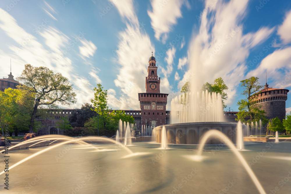 Main entrance to the Sforza Castle - Castello Sforzesco and fountain in front of it,long exposure photo, sunny day and clouds in the sky,Milan, Italy