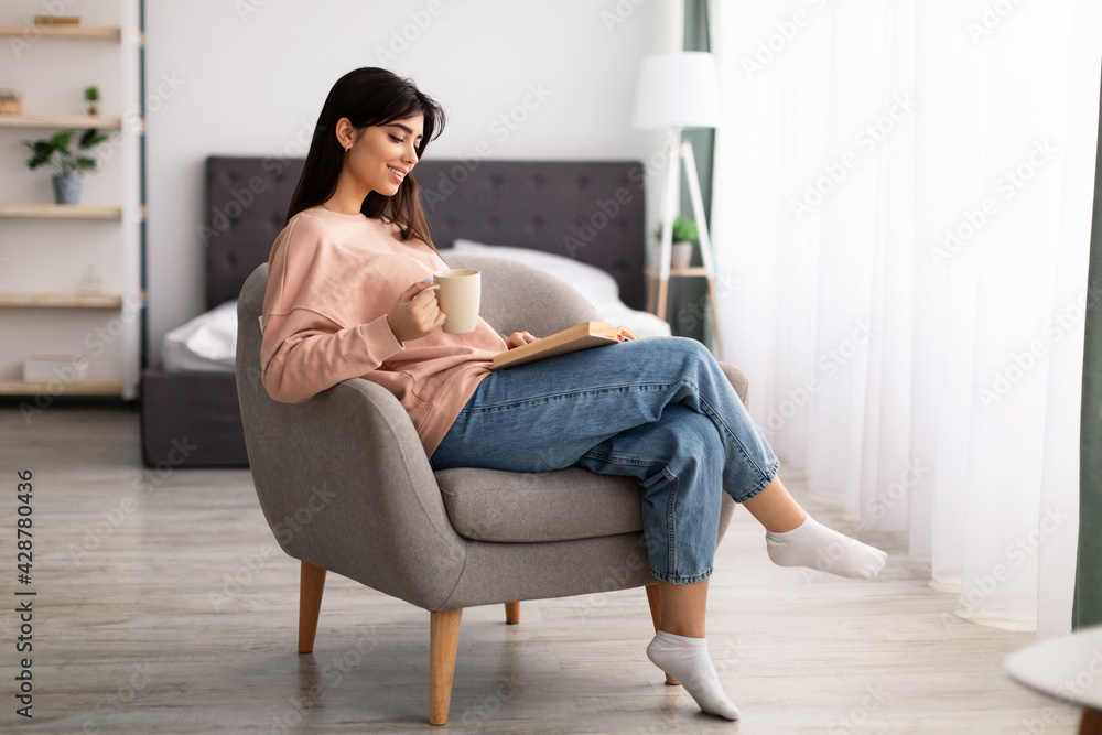 Woman having rest at home, drinking coffee reading book